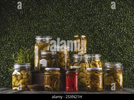 Barattoli contenenti verdure sottaceto come cetrioli, patate, peperoncino caldo e spezie, creando un'esposizione colorata e appetitosa su una linguetta di legno Foto Stock