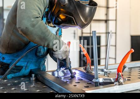 Saldatrice che unisce parti metalliche utilizzando una torcia per saldatura in officina Foto Stock