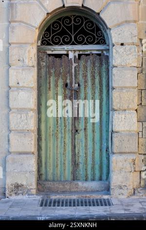 Ingresso con porta in metallo ondulato ad un edificio in pietra calcarea sull'isola di Malta. Foto Stock