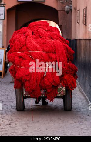 Marrakech, Marocco. Un carrello a mano carico di lana tinta rossa viene trasportato attraverso i suk centrali nella medina di Marrakech o nella città vecchia Foto Stock