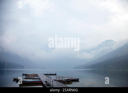 Serena nebbia mattutina appesa su un lago di montagna con barche legate ad un molo di legno Foto Stock
