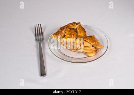 Una deliziosa torta di mele fatta in casa con crosta a reticolo seduta su un piatto di vetro con una forchetta e uno sfondo bianco. Foto Stock