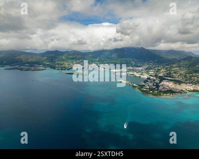 Una città costiera con baia, edifici e montagne sotto un cielo nuvoloso. Seychelles, Mahe. Foto Stock
