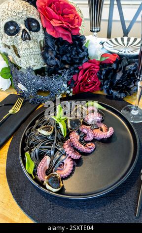 Polpo su un letto di pasta nera con inchiostro di calamaro e aglio nero su un piatto nero su un tavolo decorato per l'Ognissanti. Foto Stock