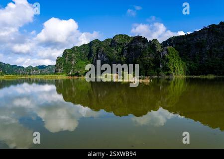 Verde paesaggio collinare del Tràng un complesso paesaggistico panoramico vicino al villaggio di Tam Cốc, riflesso nell'acqua di un fiume. Foto Stock