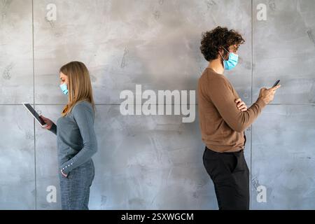 Persone in stile business e maschere mediche in piedi con gadget e mantenere la distanza sociale. Foto Stock