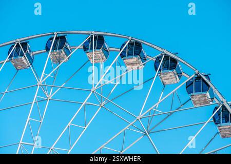 La ruota panoramica con cabine vuote offre viste mozzafiato sul parco divertimenti, promettendo un emozionante giro sotto la vasta distesa di un blu vibrante Foto Stock
