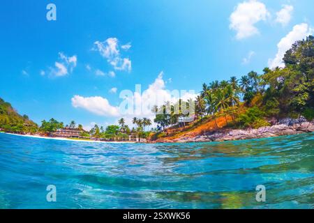 La luce del sole illumina le vibranti acque turchesi mentre le dolci onde si infrangono su una spiaggia sabbiosa circondata da torreggianti palme e da lussureggianti vegetazione Foto Stock