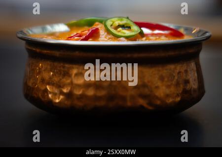 Indian Curry Dish servito in un Rustic Copper Bowl con Green Chilli Garnish Foto Stock