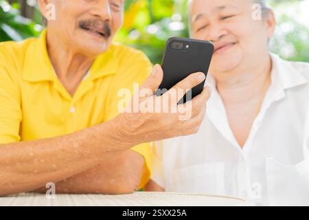 Una coppia attiva e sorridente seduto sulla sedia da giardino e guardando lo smartphone. Uso della tecnologia moderna da parte degli anziani. Foto Stock