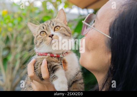 Foto di una donna asiatica matura che gioca con il suo carino gatto mentre si rilassa in giardino a casa. Messa a fuoco selettiva. Foto Stock