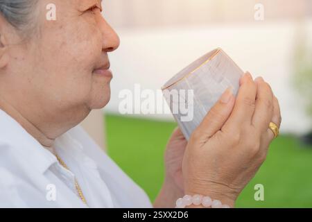 Vista verticale laterale di una donna degli anni '60 sorridente, seduta rilassante con una tazza di tè e caffè. Messa a fuoco selettiva. Foto Stock
