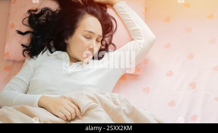 Vista dall'alto di una donna asiatica adulta in pigiama adagiata su un comodo materasso ortopedico, dorme su un morbido cuscino, godendosi una notte di dolce sogno Foto Stock