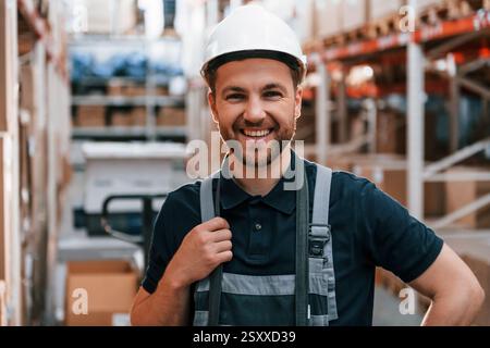 Sorridere per la fotocamera. Il dipendente in uniforme lavora nel magazzino di giorno. Foto Stock