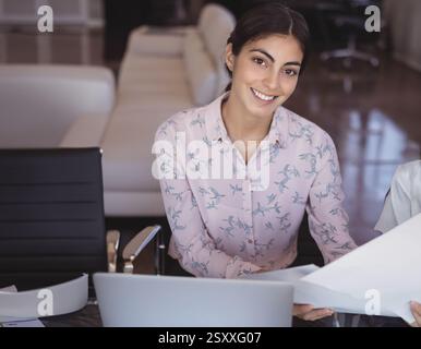 Revisione dei documenti alla scrivania dell'ufficio, donna d'affari con notebook sorridente Foto Stock