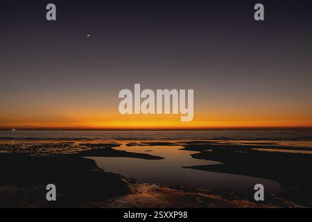 Uno splendido tramonto sulla Baia del Bengala, con il cielo che si illumina in ricche sfumature di arancio, oro e viola intenso mentre il sole tramonta dietro l'orizzonte. Foto Stock
