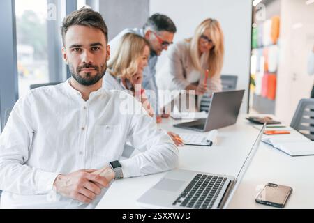 Un giovane uomo alla moda sta lavorando. Un gruppo di professionisti è in ufficio. Foto Stock