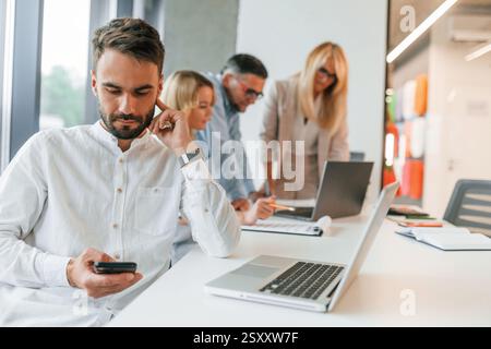 Un giovane uomo alla moda sta lavorando. Un gruppo di professionisti è in ufficio. Foto Stock