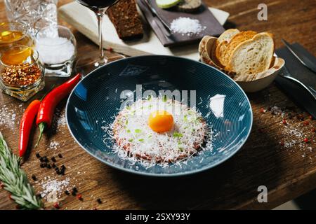 Tartare artigianale di manzo coronata da tuorlo d'uovo crudo e scaglie di parmigiano. Accompagnato da pane tostato, peperoncino rosso e rosmarino. A. Foto Stock