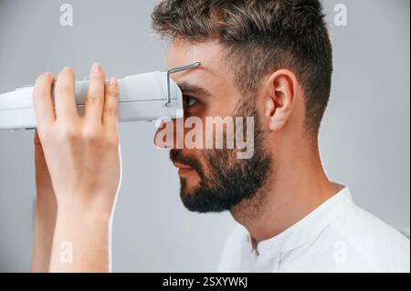 Vista laterale. Visione dell'uomo controllata dal medico in clinica utilizzando uno speciale dispositivo optometrico. Foto Stock