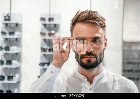 Primo piano verticale. Uomo elegante con barba che sceglie gli occhiali nel negozio di ottica. Foto Stock