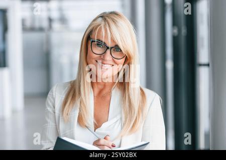 Bel ritratto. La donna in abiti formali bianchi è in piedi all'interno. Foto Stock