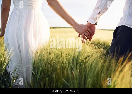 Tenersi per mano. Coppia appena sposata. Insieme sul maestoso campo agricolo nelle giornate di sole. Foto Stock