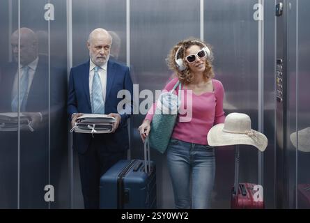 Viaggiatrice felice con bagagli e un uomo d'affari triste e annoiato che tiene i documenti, si trova in ascensore Foto Stock