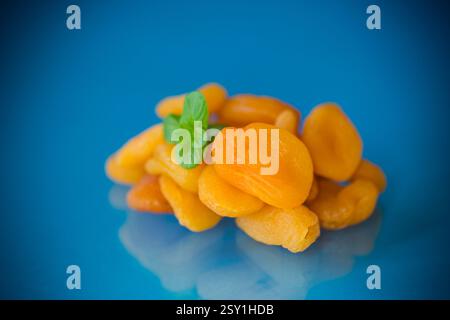 Una manciata di albicocche essiccate all'arancia brillante con un rametto di menta su sfondo blu. Foto Stock