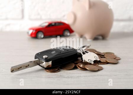 Chiave e monete dell'auto su un tavolo di legno chiaro, primo piano. Comprare auto Foto Stock