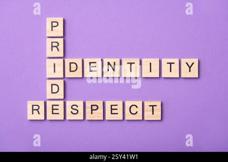 Pezzi di legno con lettere che formano un puzzle di parole incrociate con le parole orgoglio, identità, rispetto, su sfondo viola. Potente immagine concettuale di Foto Stock