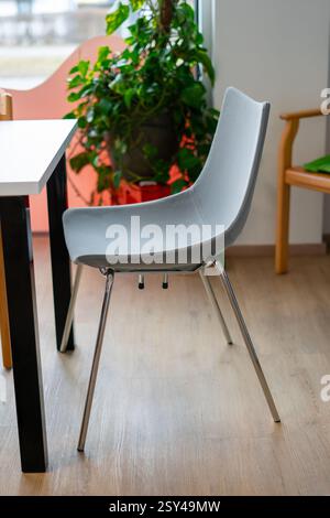 Vista di una moderna sedia grigia vicino a un tavolo in un ufficio Foto Stock