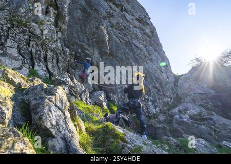 Due arrampicatrici che scalano una ripida parete rocciosa, illuminate dalla luce del sole, mostrando il lavoro di squadra e la determinazione nell'avventura all'aria aperta Foto Stock