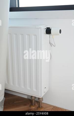 Nascondere i tubi del radiatore. Riscaldamento a radiatore bianco con termostato per risparmiare energia in casa e tubi di calore nascosti sotto il pavimento Foto Stock