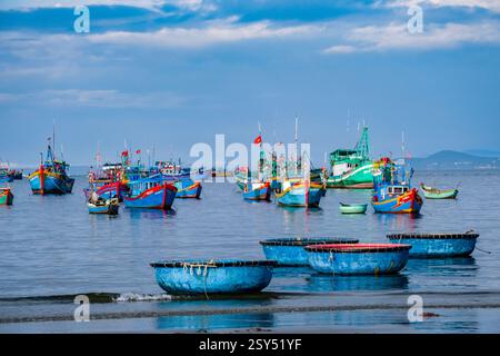 Barche tradizionali, in plastica, ancorate di fronte alla spiaggia di Mui ne, Mũi ne, molte barche da pesca in lontananza. Foto Stock