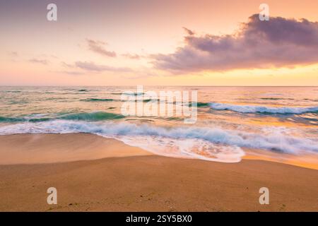vacanze estive al mare. avventura all'aria aperta. bellissimo paesaggio marino rosa viola all'alba. le onde calme bagnano la spiaggia di sabbia dorata. soffici nuvole su Foto Stock