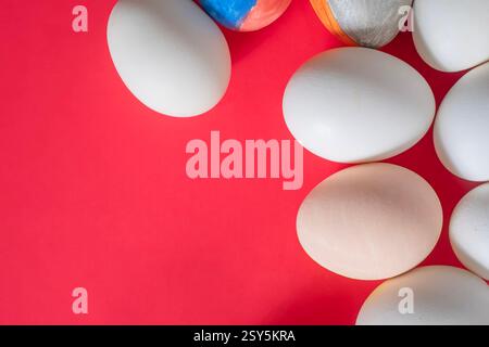 Le uova di Pasqua di vari colori, tra cui bianco semplice e splendidamente dipinte, sono ambientate su un vivace sfondo rosso. Foto Stock