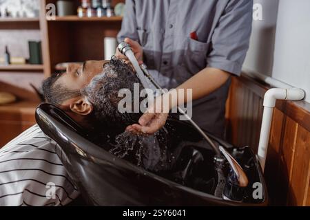 Un barbiere sta sapientemente lavando i capelli dei clienti in un ambiente elegante e moderno Foto Stock