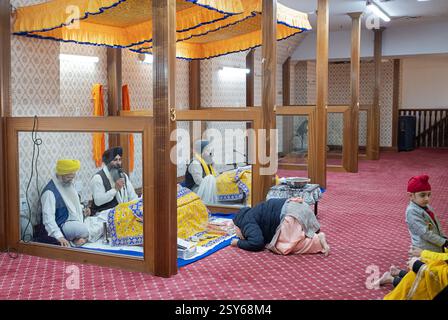 Entrando in un'area in un tempio Sikh dove viene letto il loro libro sacro, una donna Sikh più anziana si inchina mostrando rispetto e devozione. A New York. Foto Stock