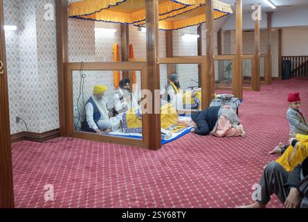 Entrando in un'area in un tempio Sikh dove viene letto il loro libro sacro, una donna Sikh più anziana si inchina mostrando rispetto e devozione. A New York. Foto Stock