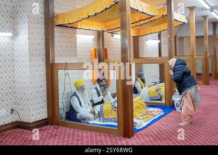 Entrando in un'area in un tempio Sikh dove viene letto il loro libro sacro, una donna Sikh più anziana a piedi nudi mostra il suo rispetto e devozione. A New York. Foto Stock