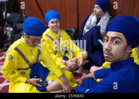 4 ragazzi attendono l'inizio di Gatka, un tradizionale concorso di arti marziali religiose in un tempio a South Richmond Hill, Queens, New York. Foto Stock