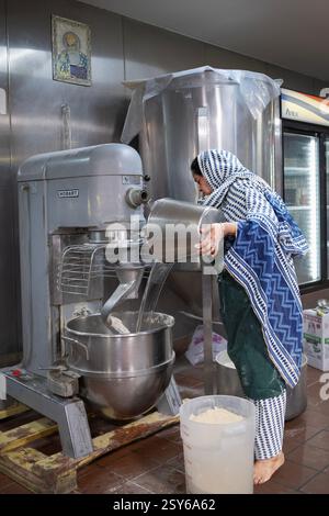 Il volontario Sikh versa acqua in una macchina per il pane per preparare il pane roti da servire in una cucina comune gratuita di langar. A New York. Foto Stock