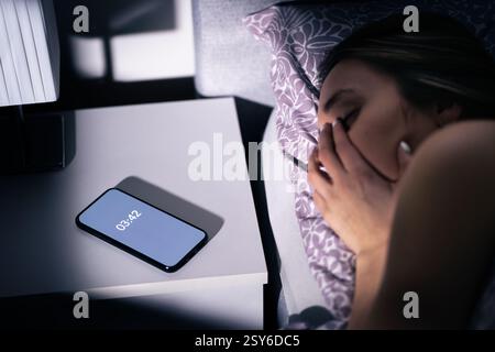 Sonno e insonnia. Donna con apnea o disturbo di notte. Persona insonne con ansia e problemi. Sveglia nel telefono sul tavolo. Foto Stock