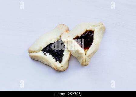 Due tradizionali biscotti hamantaschen ripieni di pasta di mohn (pasta di semi di papavero) e marmellata di prugne per il festival ebraico di Purim su una tavola di legno bianco. Foto Stock