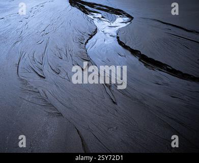 Un piccolo fiume che si fa strada attraverso una spiaggia con la bassa marea lasciando motivi nella sabbia, preso a Dunraven Bay, Glamorgan Heritage Coast, Galles. Foto Stock