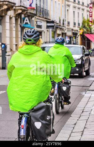 Abbinando un abbigliamento ra-wear colorato di sicurezza verde brillante in bicicletta lungo la strada del centro città - Tours, Indre-et-Loire (37), Francia. Foto Stock