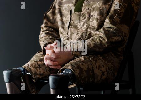 Soldato con protesi delle gambe bioniche in uniforme mimetica militare che riposa su una sedia. Foto Stock