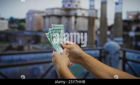Uomo che tiene in mano banconote cinesi in yuan di fronte all'architettura antica al foro romano che mette in evidenza la finanza globale all'aperto. Foto Stock