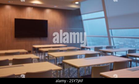 Ambiente sfocato e defocato con scrivanie vuote e un grande schermo interno, che offre uno spazio conferenze moderno e minimalista con ampio spazio naturale Foto Stock